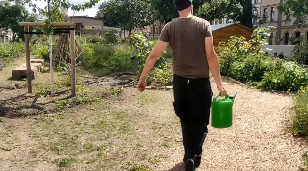 Ein Gärtner trägt eine volle Gießkanne durch den Garten auf der Gehestrasse in Dresden Pieschen.